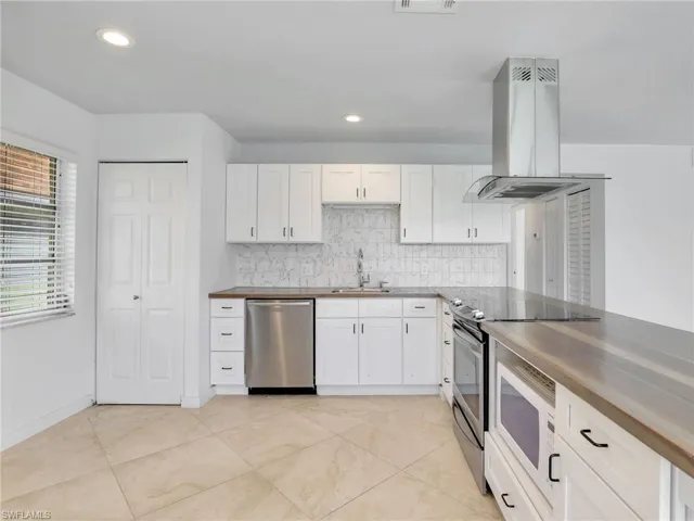 Kitchen featuring stainless steel appliances, island exhaust hood, decorative backsplash, white cabinets, and wood counters