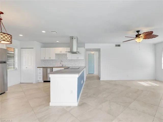 Kitchen featuring plenty of natural light, white cabinets, island exhaust hood, appliances with stainless steel finishes, and recessed lighting