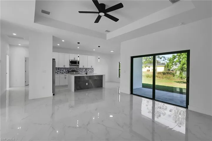 Unfurnished living room with light marble finish flooring, a raised ceiling, and a ceiling fan