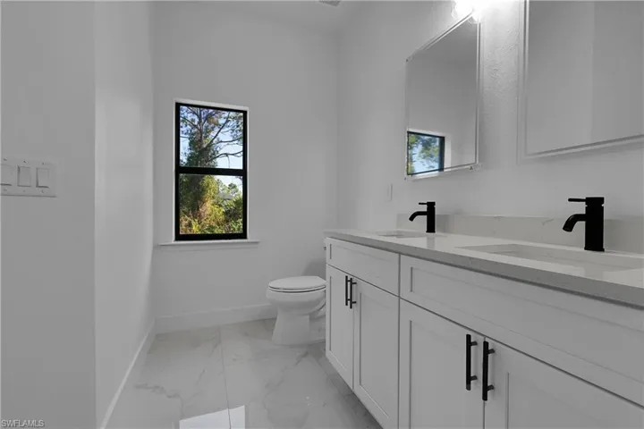 Full bath featuring double vanity and light marble finish flooring