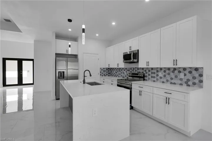Kitchen featuring stainless steel appliances, white cabinets, decorative light fixtures, light stone counters, and light marble finish floors