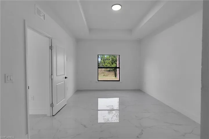 Unfurnished bedroom with light marble finish flooring and a raised ceiling