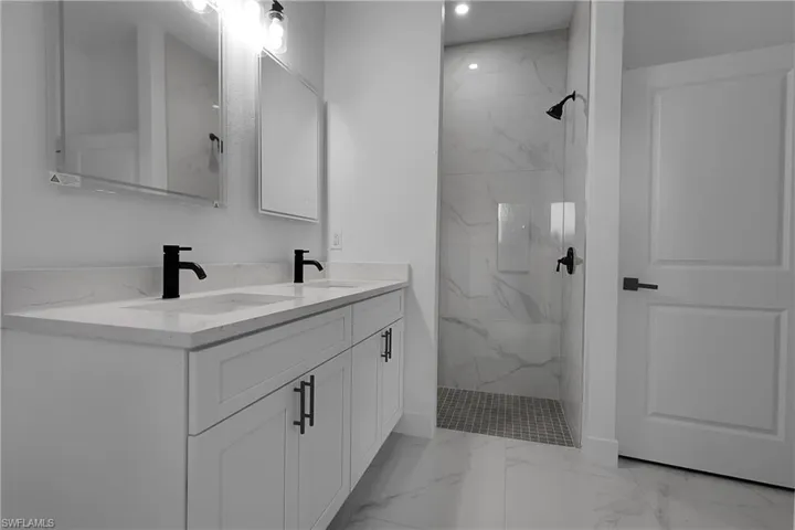 Bathroom featuring light marble finish floors, double vanity, and a marble finish shower
