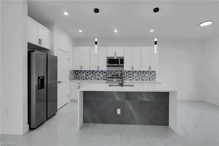 Kitchen featuring light stone counters, appliances with stainless steel finishes, pendant lighting, and recessed lighting