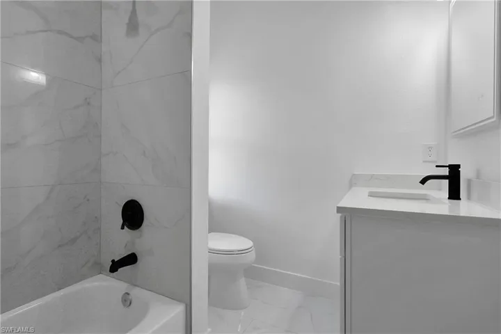 Bathroom featuring vanity, light marble finish floors, and washtub / shower combination