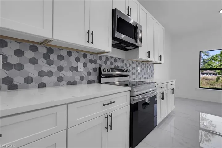 Kitchen with appliances with stainless steel finishes, white cabinets, light marble finish flooring, and tasteful backsplash