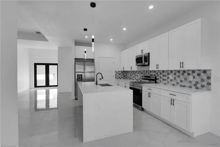 Kitchen featuring appliances with stainless steel finishes, white cabinetry, light stone counters, pendant lighting, and light marble finish flooring
