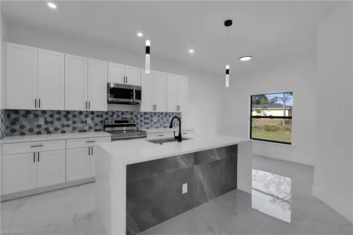 Kitchen with light marble finish flooring, recessed lighting, decorative light fixtures, appliances with stainless steel finishes, and backsplash
