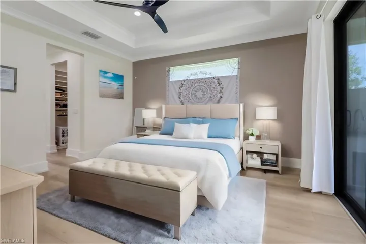 Master bedroom, featuring custom his and her walk in closets, tray ceiling, and sliding glass doors to the screened lanai. Image virtually staged.