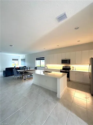 Kitchen featuring white cabinetry, light tile patterned floors, stainless steel appliances, a kitchen island with sink, and sink