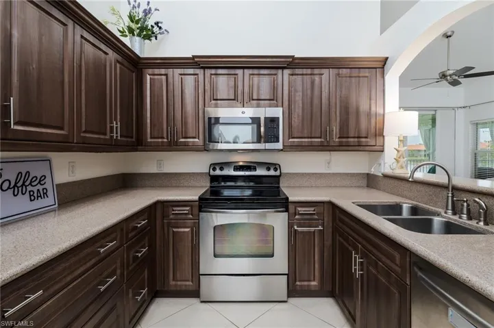 Kitchen with stainless steel appliances, a ceiling fan, light tile patterned floors, dark brown cabinets, and light countertops