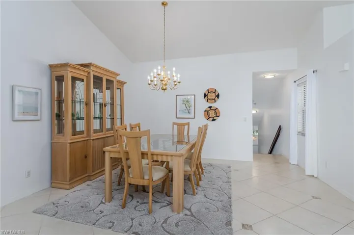 Dining area with light tile patterned floors, lofted ceiling, and a chandelier