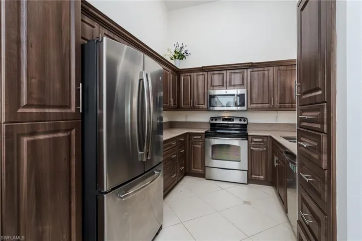 Kitchen featuring appliances with stainless steel finishes, light countertops, light tile patterned flooring, and dark brown cabinetry