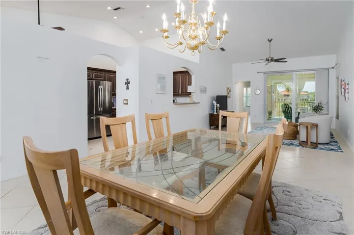 Dining area featuring vaulted ceiling, arched walkways, light tile patterned flooring, a ceiling fan, and a chandelier