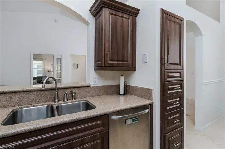 Kitchen with stainless steel dishwasher, arched walkways, light tile patterned flooring, and dark brown cabinetry