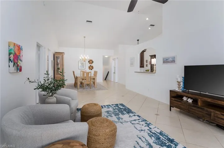 Living area with light tile patterned floors, a chandelier, a ceiling fan, and high vaulted ceiling