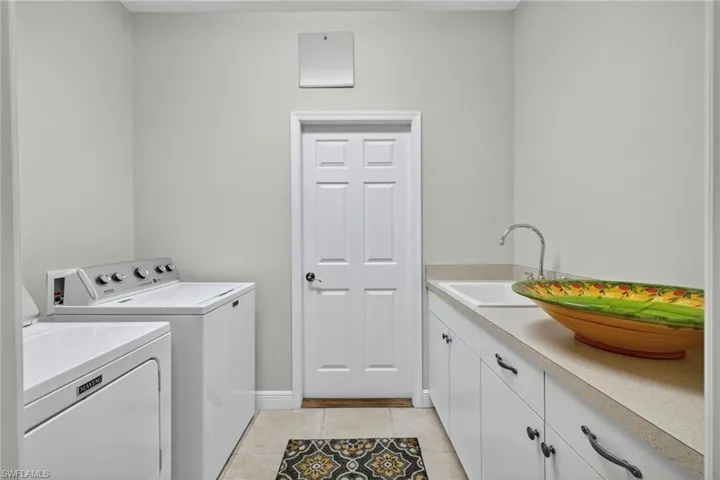 Washroom featuring washing machine and clothes dryer, light tile patterned floors, and cabinet space