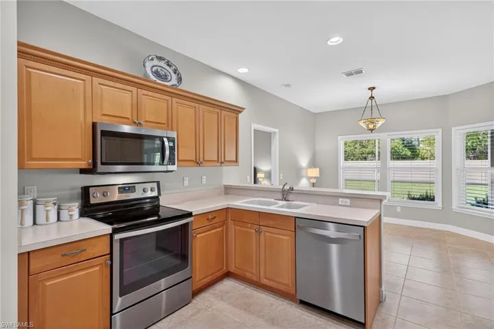 Kitchen with stainless steel appliances, light countertops, recessed lighting, light tile patterned floors, and a peninsula