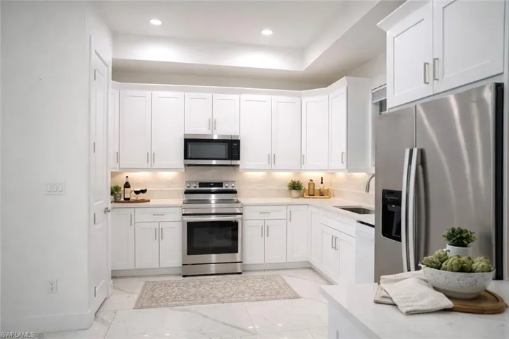 Kitchen featuring stainless steel appliances, white cabinets, light marble finish floors, recessed lighting, and light stone countertops