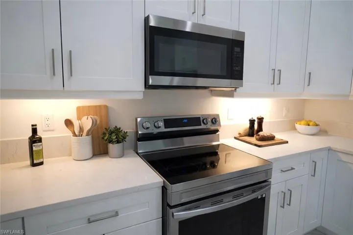 Kitchen featuring stainless steel appliances, white cabinetry, and light stone counters