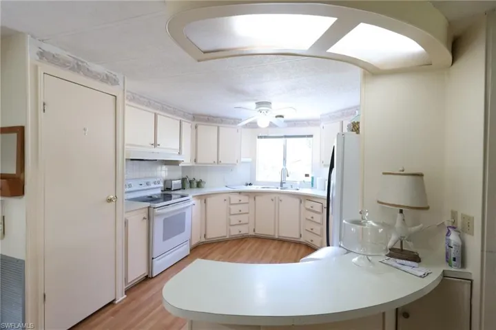 Kitchen featuring light wood-type flooring, white appliances, white cabinets, sink, and tasteful backsplash