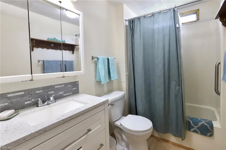 Full bathroom with shower / bath combination with curtain, backsplash, toilet, and large vanity