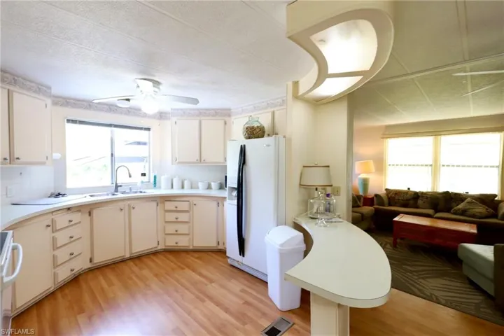 Kitchen with ceiling fan, light hardwood / wood-style floors, white fridge with ice dispenser, backsplash, and sink