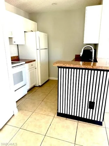 Kitchen with white cabinetry, dark countertops, white electric stove, light tile patterned floors, and a textured ceiling