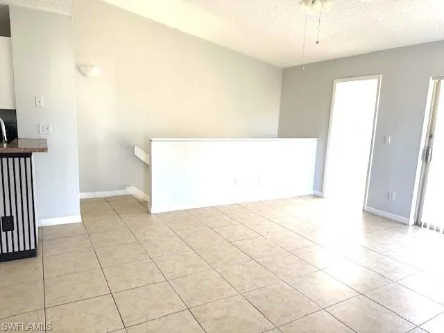 Empty room featuring a textured ceiling, light tile patterned floors, and a ceiling fan