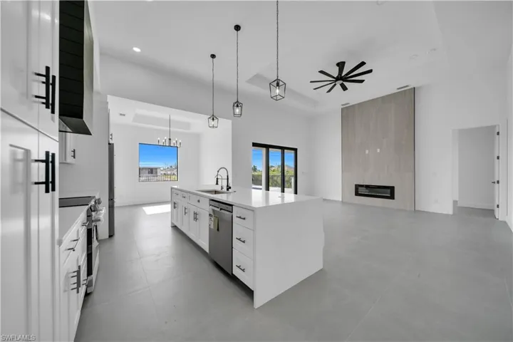 Kitchen with ceiling fan, a tray ceiling, white cabinetry, a center island with sink, and a fireplace