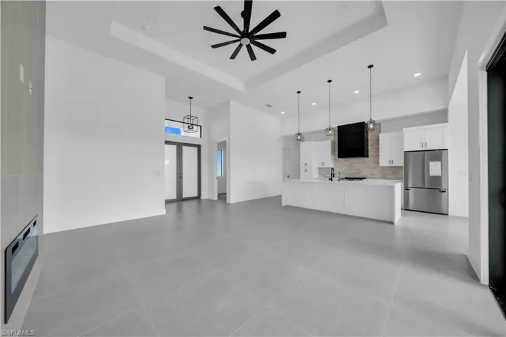 Unfurnished living room with a ceiling fan, a high ceiling, recessed lighting, a raised ceiling, and light tile patterned floors