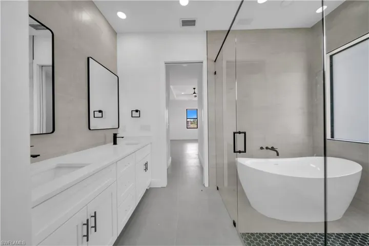 Bathroom featuring a soaking tub, double vanity, a shower stall, recessed lighting, and tile walls