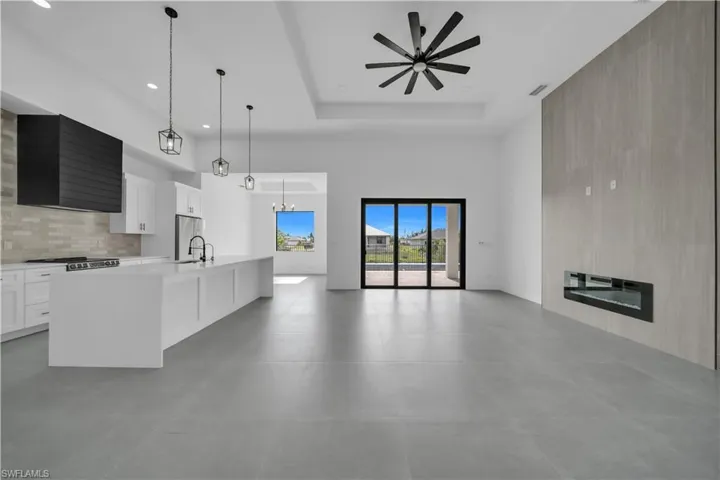 Kitchen featuring open floor plan, ceiling fan, light countertops, a kitchen island with sink, and white cabinetry