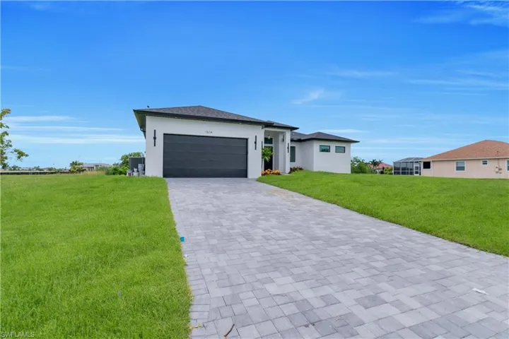 Prairie-style home with a garage, a front lawn, stucco siding, and decorative driveway