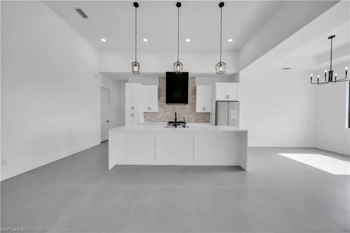 Kitchen featuring white cabinets, backsplash, stainless steel fridge, a large island with sink, and recessed lighting