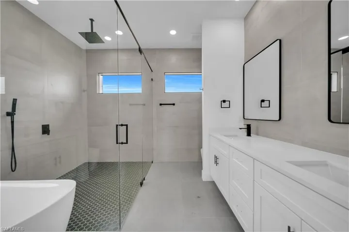 Bathroom with a shower stall, recessed lighting, double vanity, a freestanding tub, and tile walls