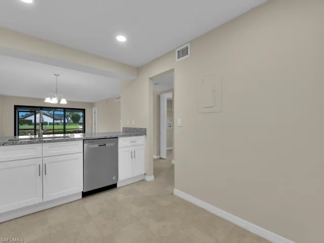 Kitchen featuring visible vents, light stone counters, white cabinetry, an inviting chandelier, and dishwasher