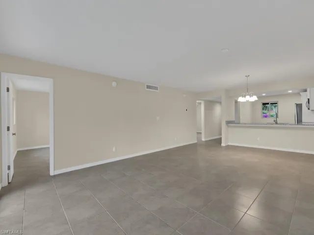 Unfurnished living room featuring tile patterned floors, a notable chandelier, baseboards, and visible vents