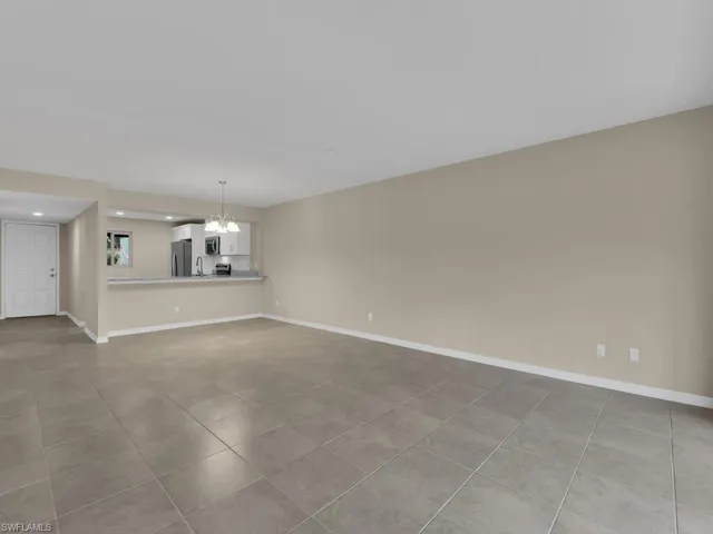 Unfurnished living room featuring an inviting chandelier, baseboards, and tile patterned floors