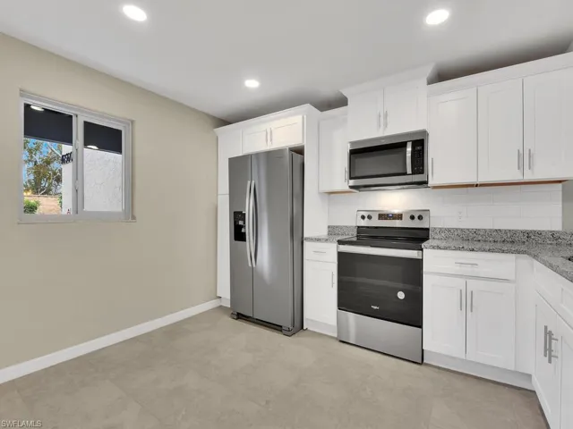 Kitchen with baseboards, light stone counters, decorative backsplash, appliances with stainless steel finishes, and white cabinetry