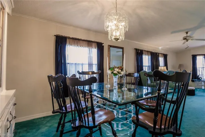 Dining space featuring ornamental molding, a textured ceiling, ceiling fan with notable chandelier, and dark colored carpet