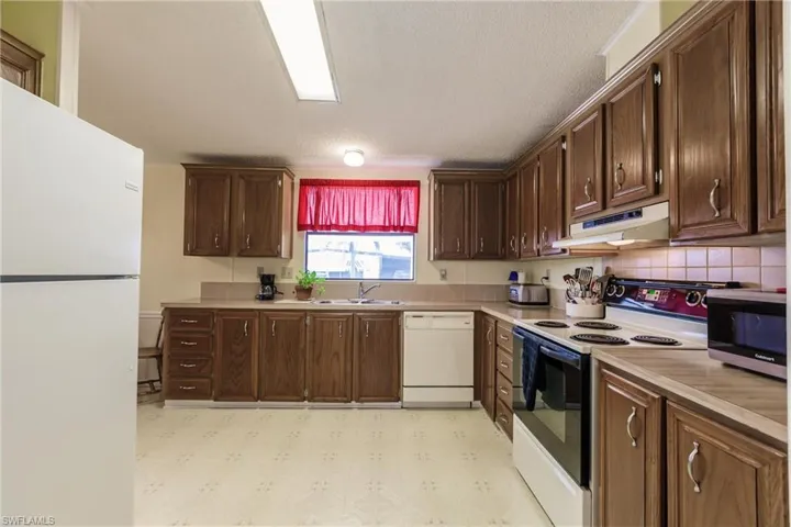 Kitchen featuring a textured ceiling, sink, dark brown cabinets, and white appliances