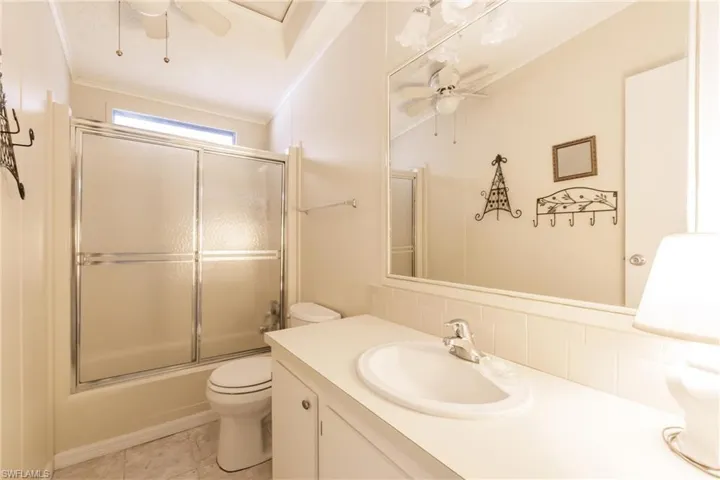 Full bathroom featuring decorative backsplash, enclosed tub / shower combo, ceiling fan, toilet, and vanity