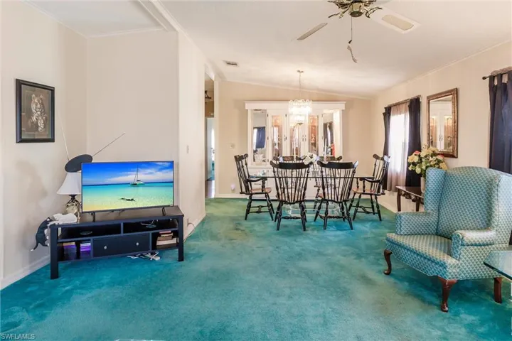 Carpeted dining area with lofted ceiling, ornamental molding, and ceiling fan with notable chandelier