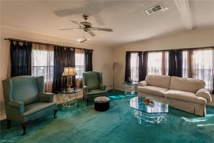 Living room featuring ceiling fan, a textured ceiling, carpet floors, and vaulted ceiling with beams