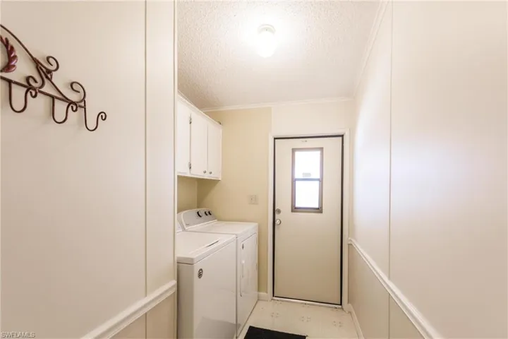 Clothes washing area with crown molding, washer and dryer, a textured ceiling, and cabinets
