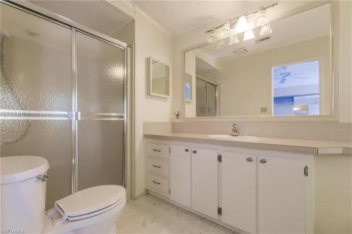 Bathroom featuring a textured ceiling, toilet, ceiling fan, walk in shower, and vanity