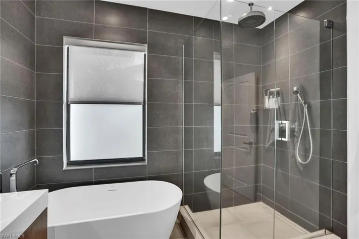 Full bathroom featuring a freestanding tub, tile walls, tiled shower, and vanity