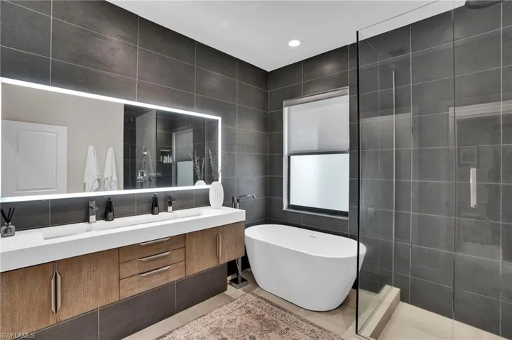Bathroom featuring tile walls, double vanity, a freestanding bath, a tile shower, and recessed lighting