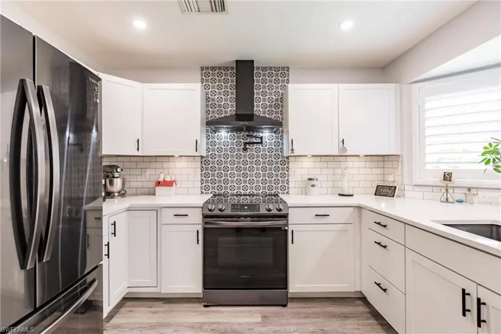Kitchen featuring stainless steel appliances, wall chimney exhaust hood, tasteful backsplash, and white cabinets
